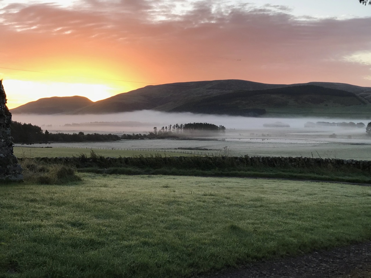Dramatic sunrise over the Medwin valley with ground mist rising from the fields and the silhouette of a stone ruin on the left edge